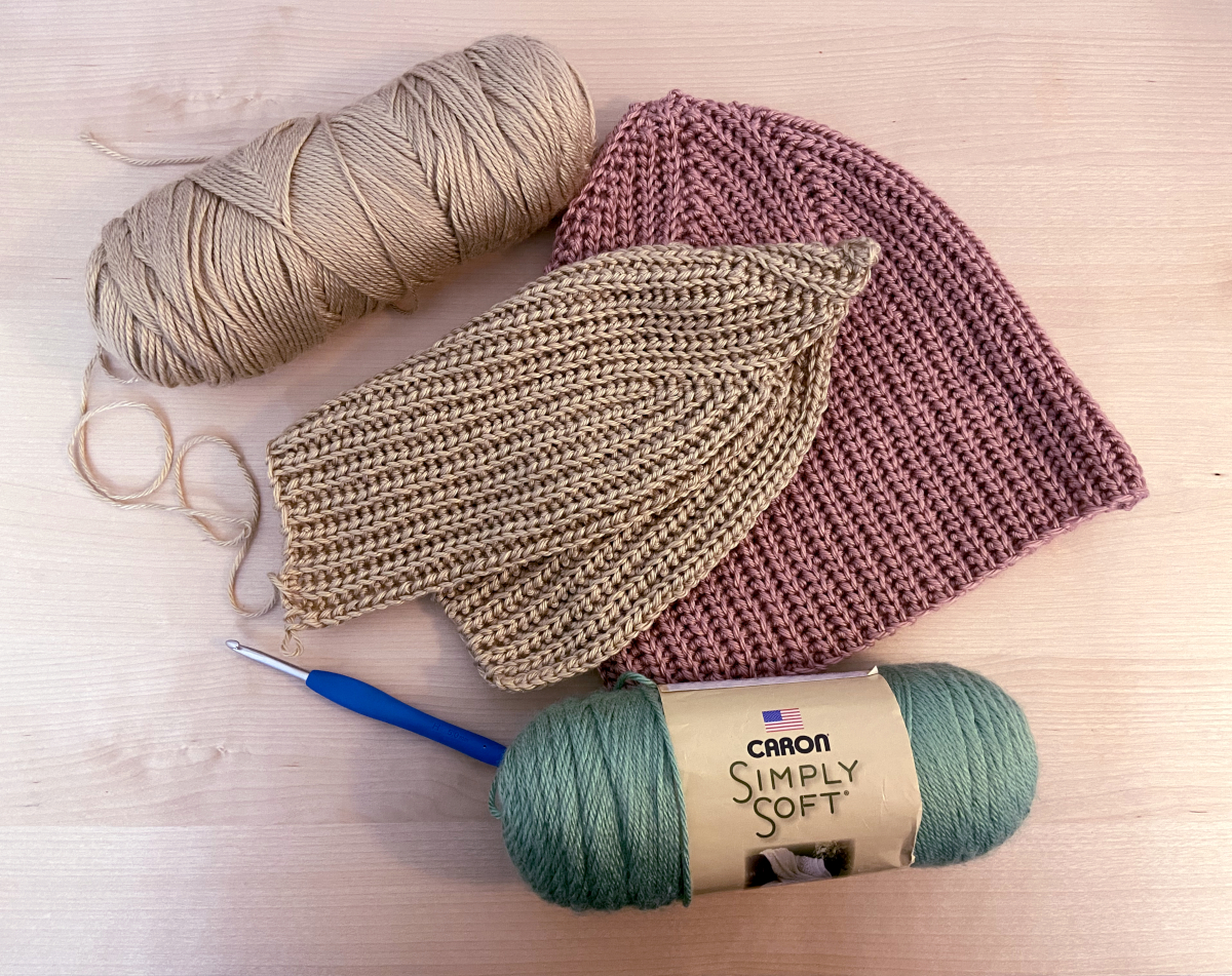 partially made crochet hat lies on top of a completed hat